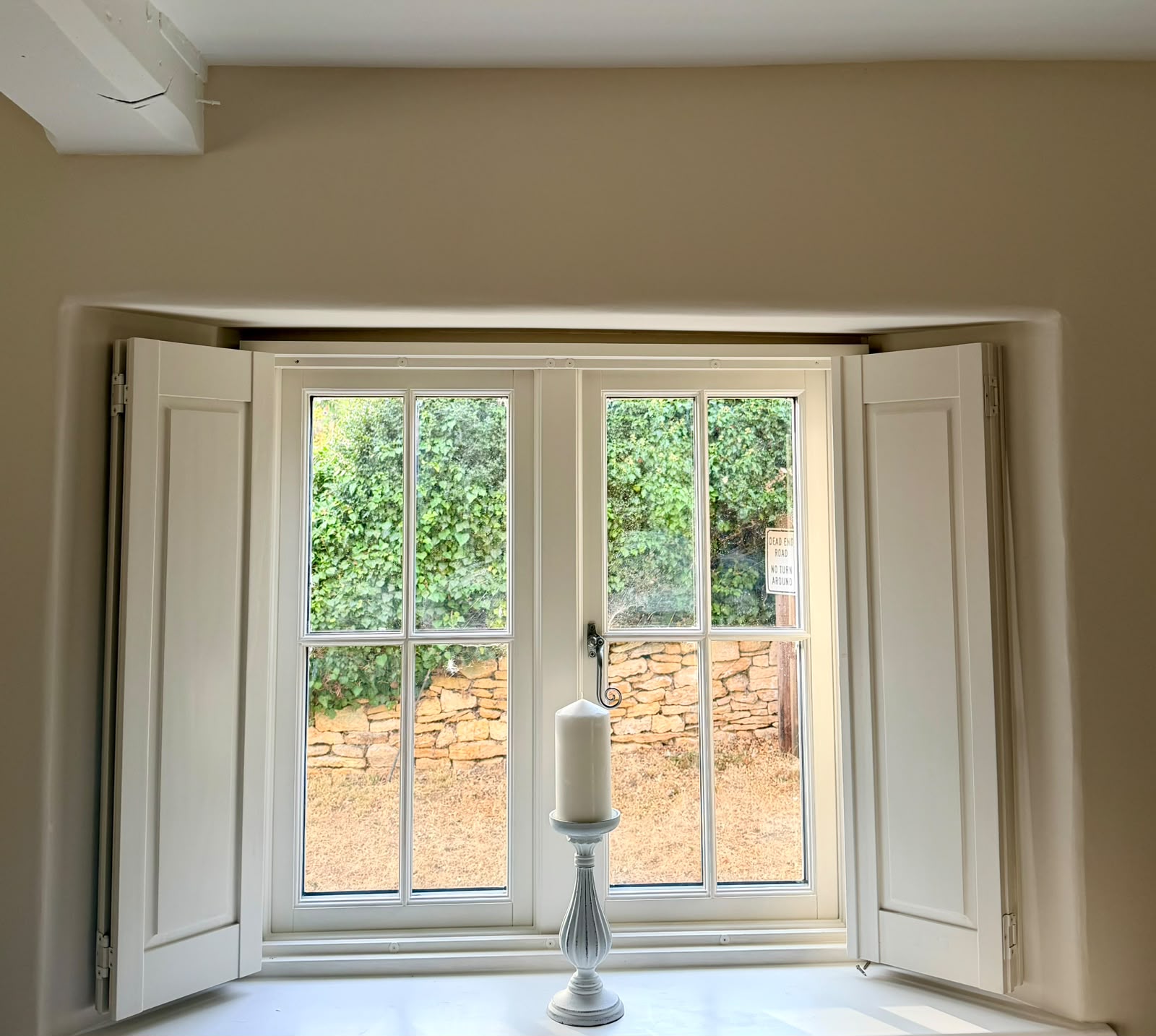 Cream-painted window surround with open shutters and a candle on the sill