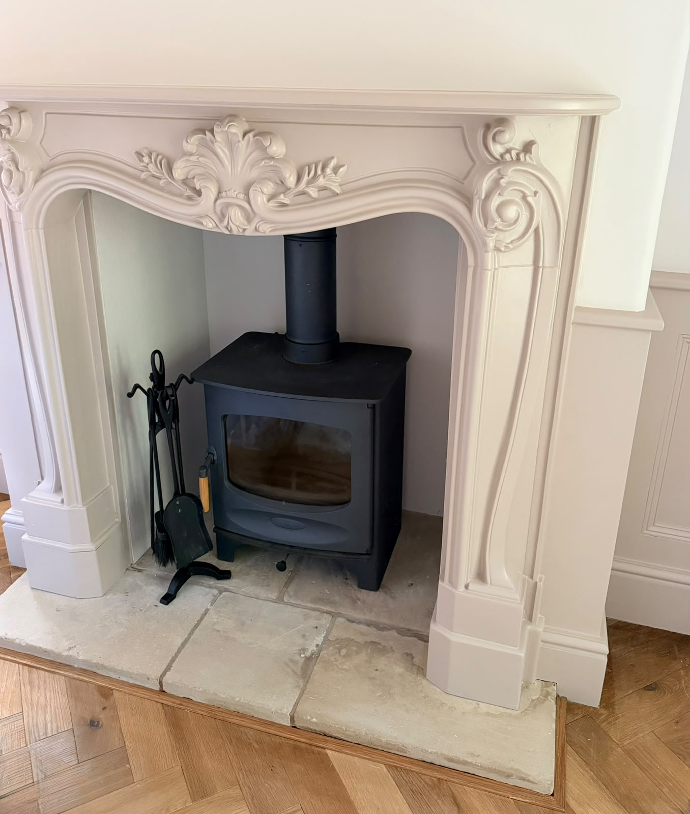 Ornate pale fireplace surround with a black stove and stone hearth