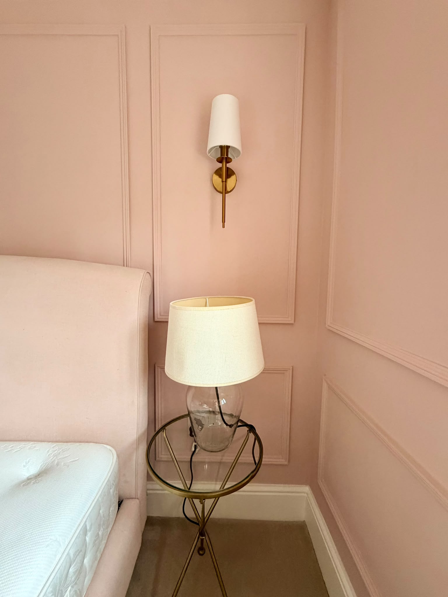 Pink wall panelling with a brass wall light and bedside lamp