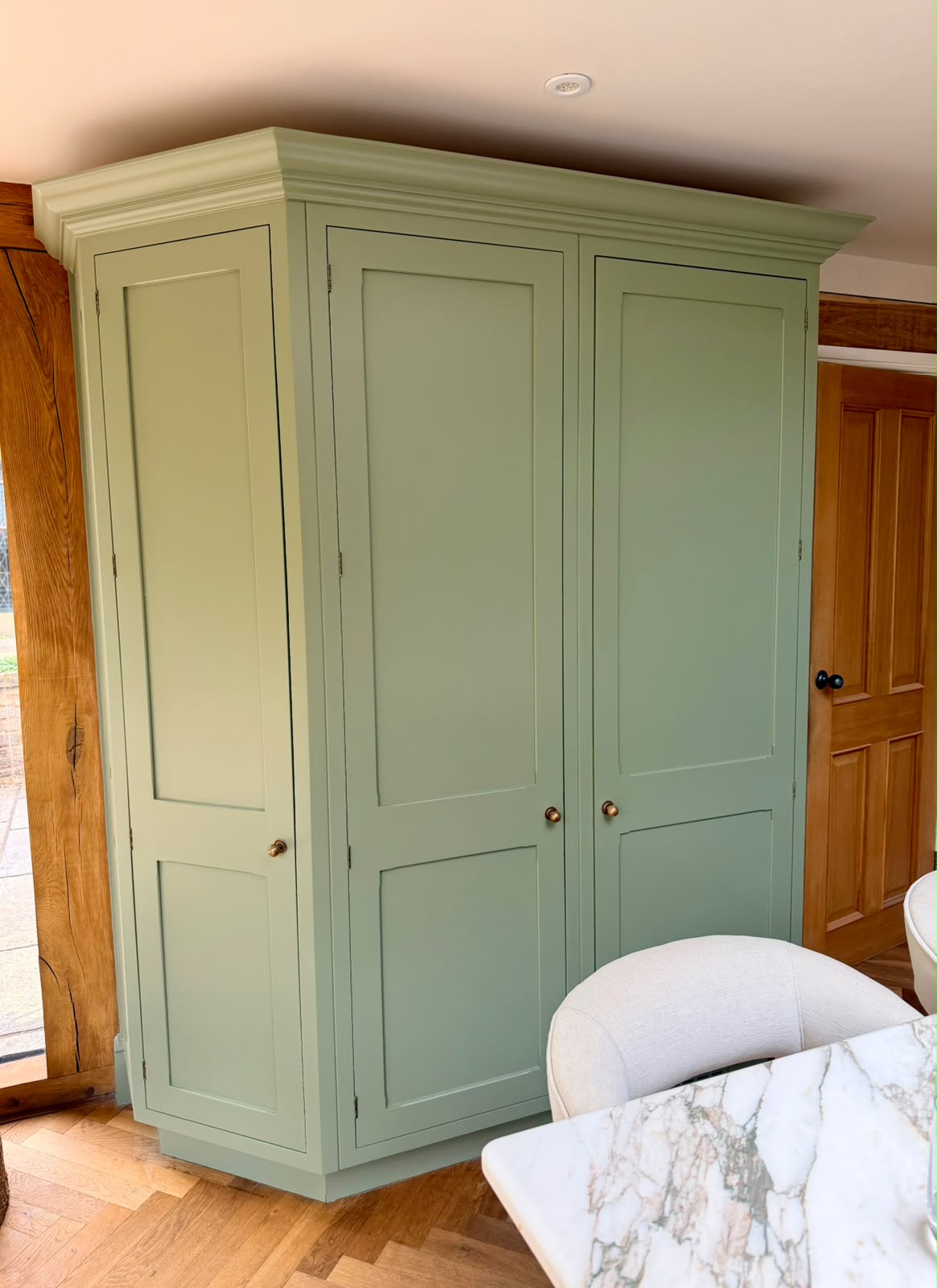 Sage-green fitted cabinetry beside a timber door and dining table