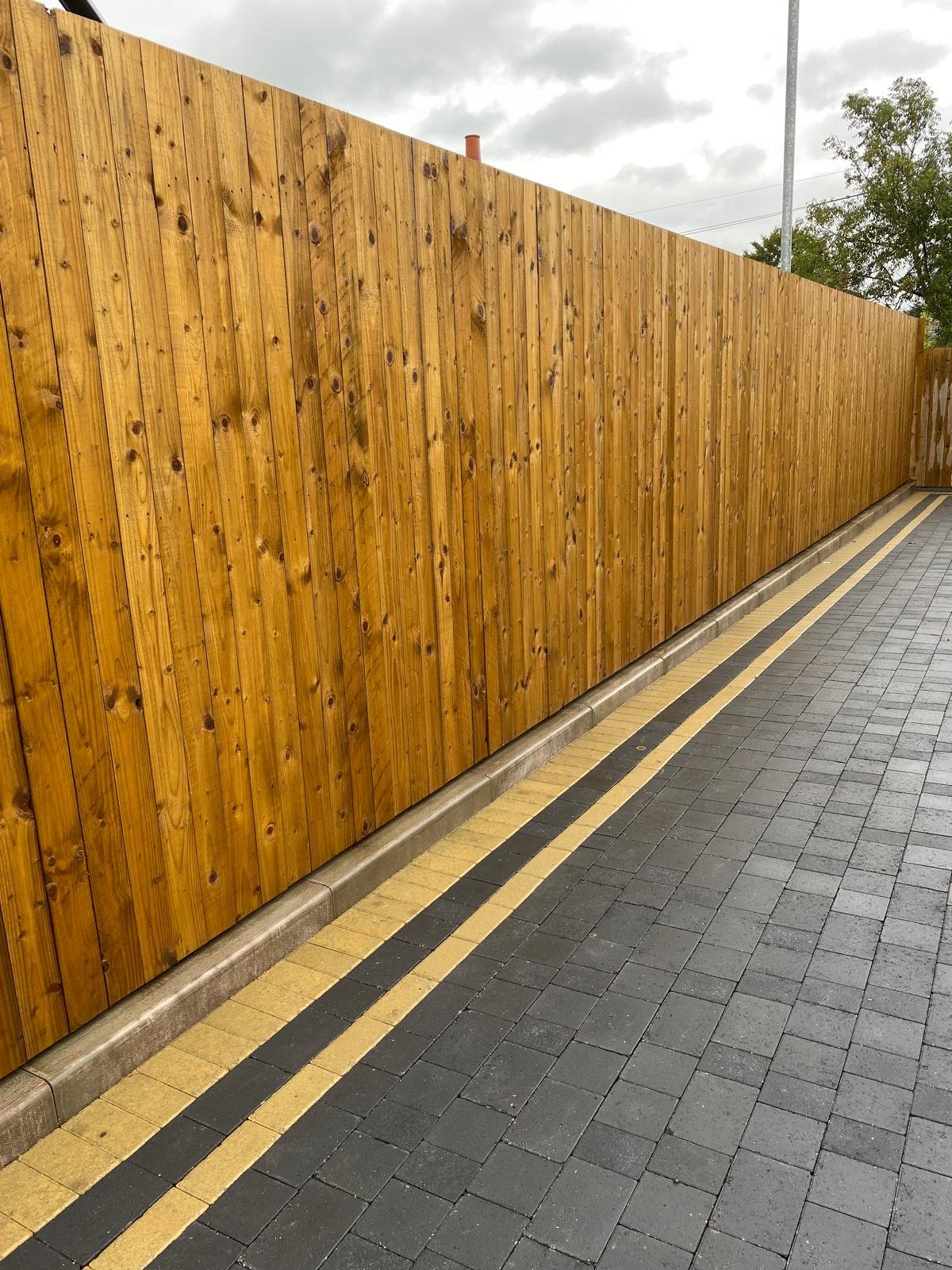 Dark block paving laid alongside a long timber boundary fence