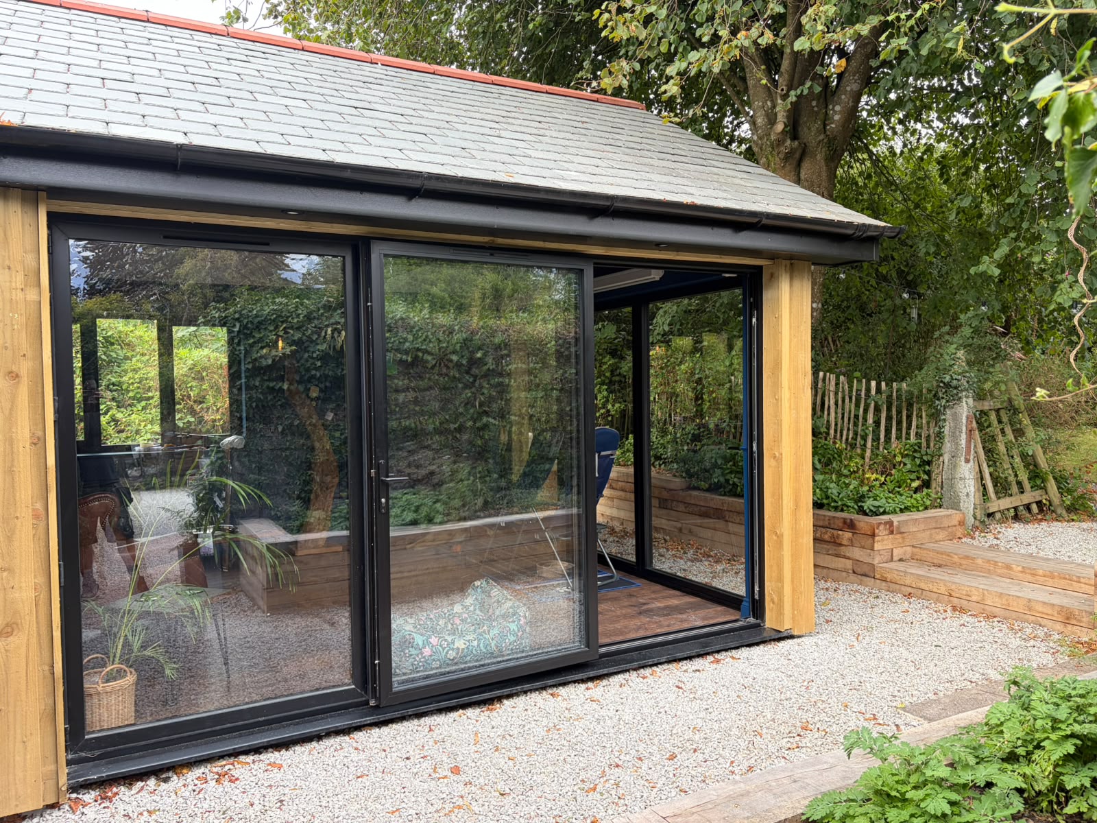Timber-clad garden pub built by our team, with black sliding glass doors and a slate roof