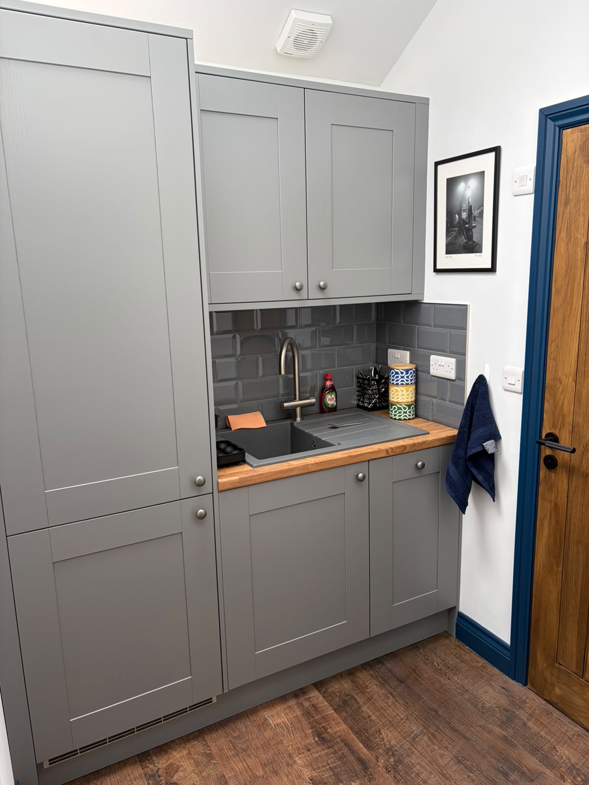 Grey fitted kitchenette with a sink, tiled splashback and timber worktop in a garage conversion
