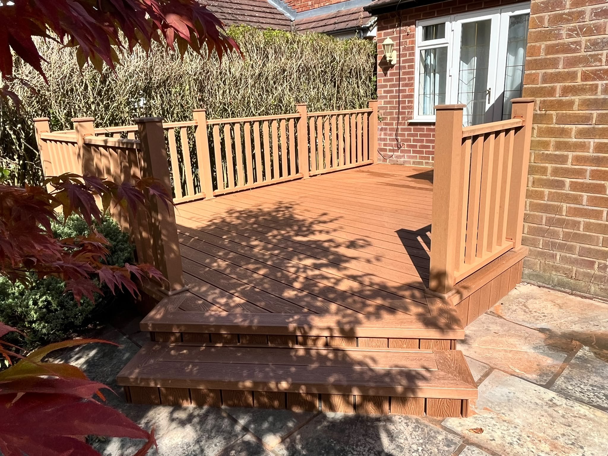 Golden-oak composite deck with a spindle balustrade and wide steps down to stone paving