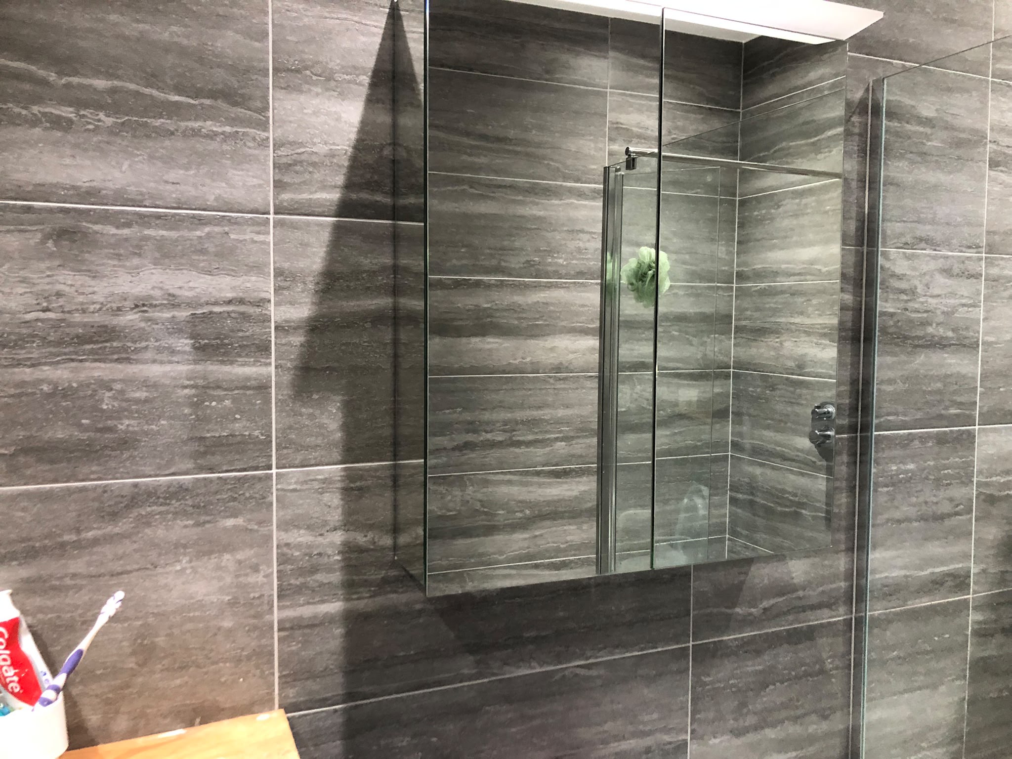 Grey tiled shower enclosure with a recessed shelf and glass screen