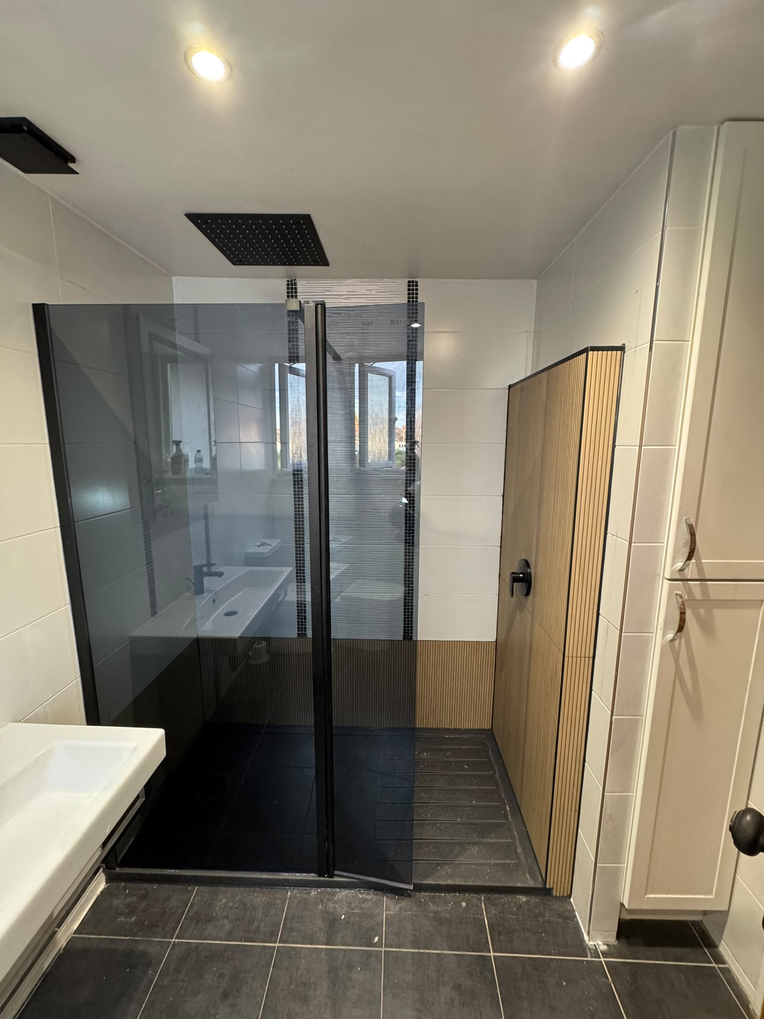 Bath to walk-in shower conversion with a black-framed smoked glass screen, ceiling rainfall shower and wood-effect fluted tiles