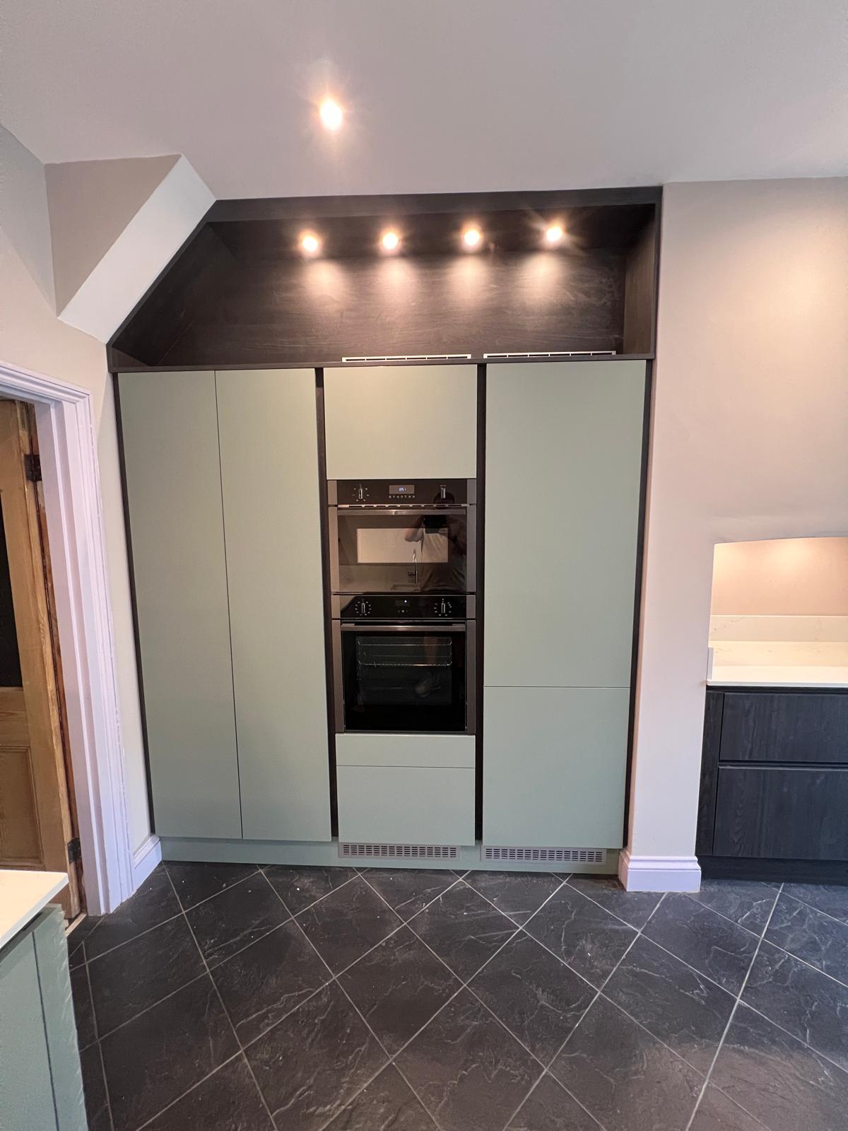 Tall sage green kitchen units with built-in double oven and downlights, fitted by Truscon