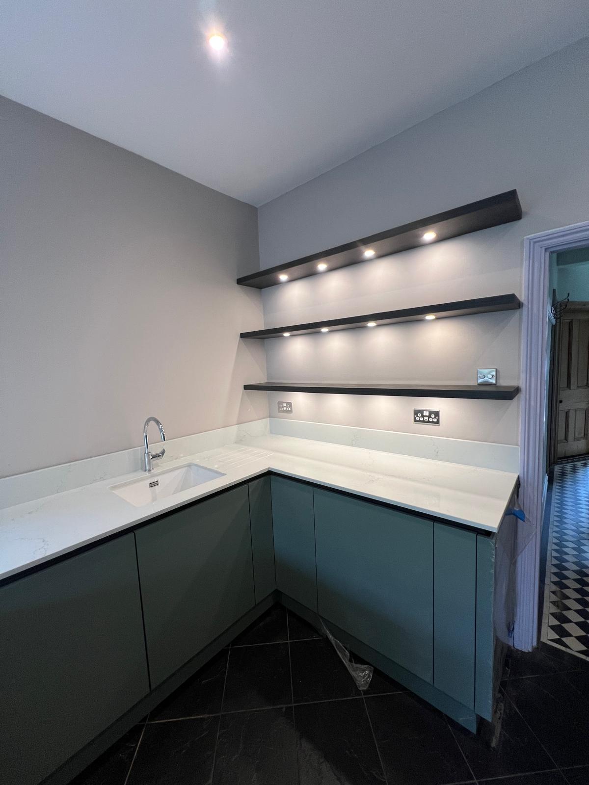 Sage green handleless kitchen with quartz worktop and lit floating shelves, fitted by Truscon